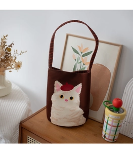 Detail of white cat embroidery on brown canvas bucket bag with red plaid handle