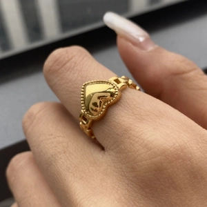 Detailed close-up of a gold heart ring with bead texture on fingers, polished metal finish
