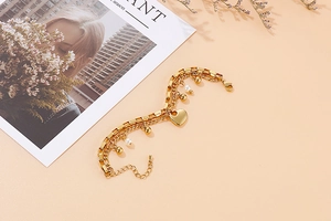 Détail d'un bracelet double rang doré avec pendentif cœur, perles polies et perles blanches
