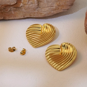Close-up of golden heart earrings with pleated texture on textured cream background