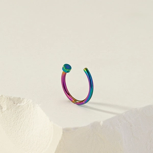 Macro shot of a rainbow metallic C-shaped non-piercing nose ring on a stone base