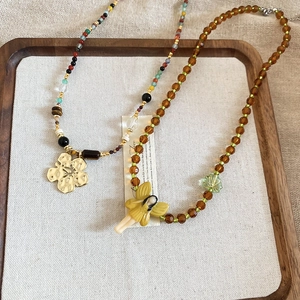 Detail of beaded necklace with gold flower pendant and yellow fairy charm on beige linen