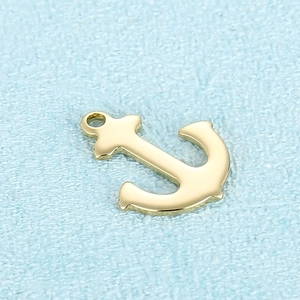 Polished golden stainless steel anchor pendant accessory on a blue textured surface