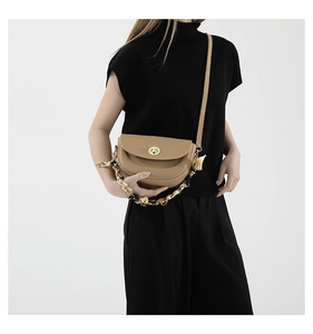 Close-up of a light brown saddle bag with gold rotating lock and silk scarf handle
