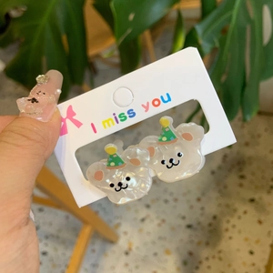 Close-up of cute pearlescent cartoon bear earrings with party hats on a card