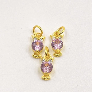 Detailed view of three gold owl pendants featuring vibrant purple crystal inlays