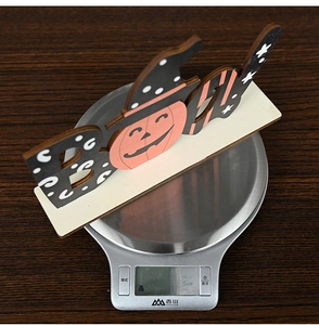 Halloween wooden BOO sign with pumpkin and wizard hat details weighing 59.7 grams on a scale