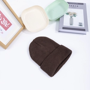 Close-up of a dark brown ribbed knit beanie hat flat laid with decorative lifestyle props