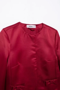 Detail of red glossy fabric neckline with bow ornament and size S label branding