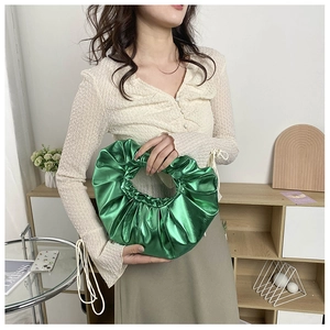 Detail einer grünen Metallic-Handtasche mit Faltenring, von einem Model in Innenräumen