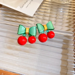 Detail von roten Kirsch-Ohrsteckern mit grünen Schleifen auf strukturierter Glasfläche