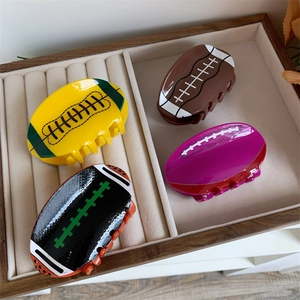 Détail de quatre pinces à cheveux en forme de rugby en acrylique sur un plateau en bois