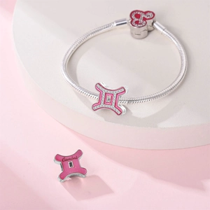 Detail of pink enamel Gemini zodiac charms on silver-plated snake chain bracelet