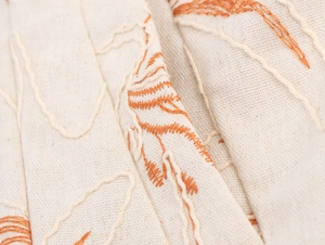 Macro view of beige cotton-linen fabric with detailed orange embroidery patterns