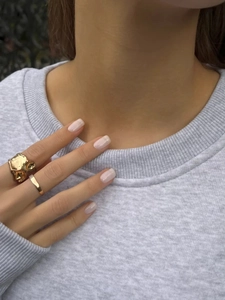 Close-up of chunky gold lava textured ring and slim band worn on hand over gray sweater