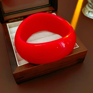 Close-up of a red irregular wave wide bangle inside a luxury wooden jewelry box