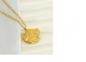 Detail of a golden fan-shaped shell pendant with sparkling rhinestones and textured surface