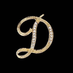 Elegant gold cursive D-shaped brooch with sparkling white rhinestones on black background