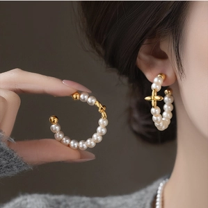 Detail of C-shaped gold-plated hoop earrings featuring pearls and a 4-petal flower