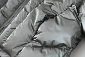 Detailed close-up of metallic silver puffer jacket with side pocket and zipper texture