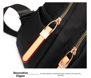 Detail of black nylon backpack featuring golden metal zippers with orange leather pull tabs