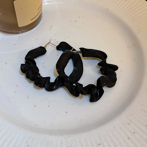 Close-up of black pleated fabric hoop earrings with silver needles on a ceramic tray