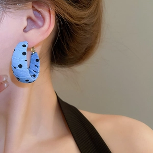Close-up of blue polka dot fabric wrapped C-shaped earrings worn by a model