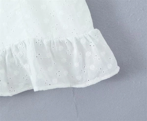 Close-up of white embroidered eyelet fabric texture with delicate lace trim details