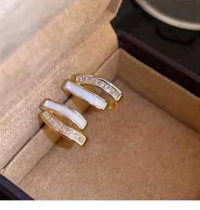 Macro shot of gold earrings with white shell inlay and zircon stones in a jewelry box