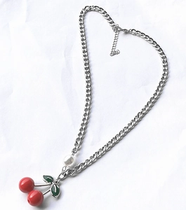 Macro detail of cherry pendant with red fruit and green leaves on silver chain