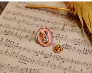 Close-up of pink oval flower brooch with rhinestones on vintage sheet music