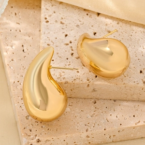 Macro shot of gold teardrop earrings with polished finish on a beige stone surface
