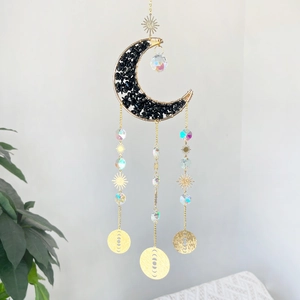 Detail of golden moon wind chime with black stones and crystal prisms in sunlight