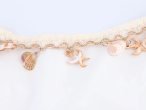 Detail of crochet lace trim with decorative seashells and starfish charms on a white dress