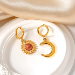 Detail of asymmetric sun and moon gold earrings with red beads on luxury silk background