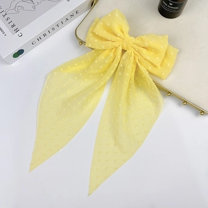 Macro detail of yellow chiffon bow hair clip with white polka dots on a vintage tray