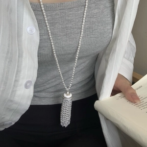 Close-up of pearl necklace featuring a tassel pendant on a model with literary aesthetic