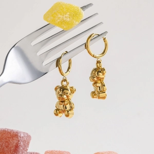 Close-up of golden bear charm hoop earrings hanging on a fork with gummy bears