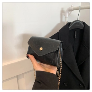 Close-up of black crocodile texture handbag with golden chain strap and buckle