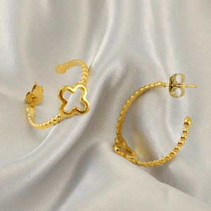 Golden hollow clover hoop earrings with beaded texture on smooth grey satin background