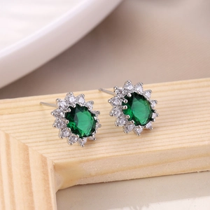 Macro detail of emerald-style stud earrings with green oval stone and zircon halo