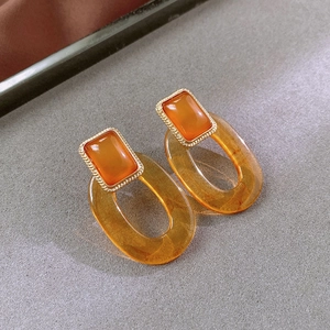 Close-up of amber resin drop earrings with golden textured metal and geometric shapes
