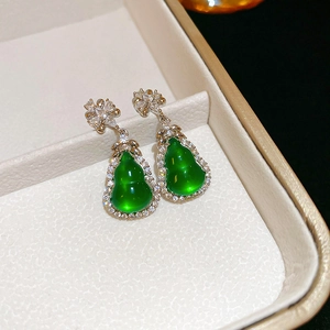 Macro shot of green gourd-shaped earrings with white zircon accents on a jewelry box