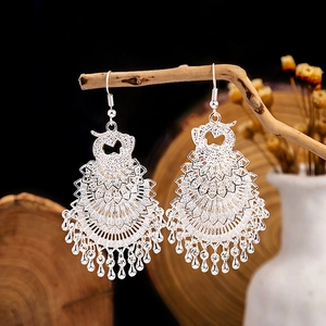 Detailed shot of ethnic silver hollow peacock earrings hanging on a rustic wooden branch
