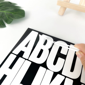 Close-up of tweezers peeling a 3-inch black and white PVC letter B sticker for DIY decor