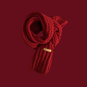 Close-up of red cable knit scarf texture featuring a handmade tag on dark red background