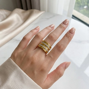 Wide gold plated stainless steel ring with rows of crystals on white marble surface