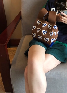 Knitted tote bag with blue and white heart patterns held by a woman on a sofa