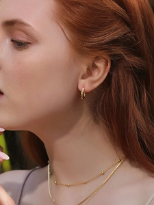 Close-up of small polished gold twisted hoop earrings worn by a female model