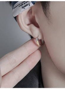 Macro shot of a silver hoop earring with gold flame details worn by a male model